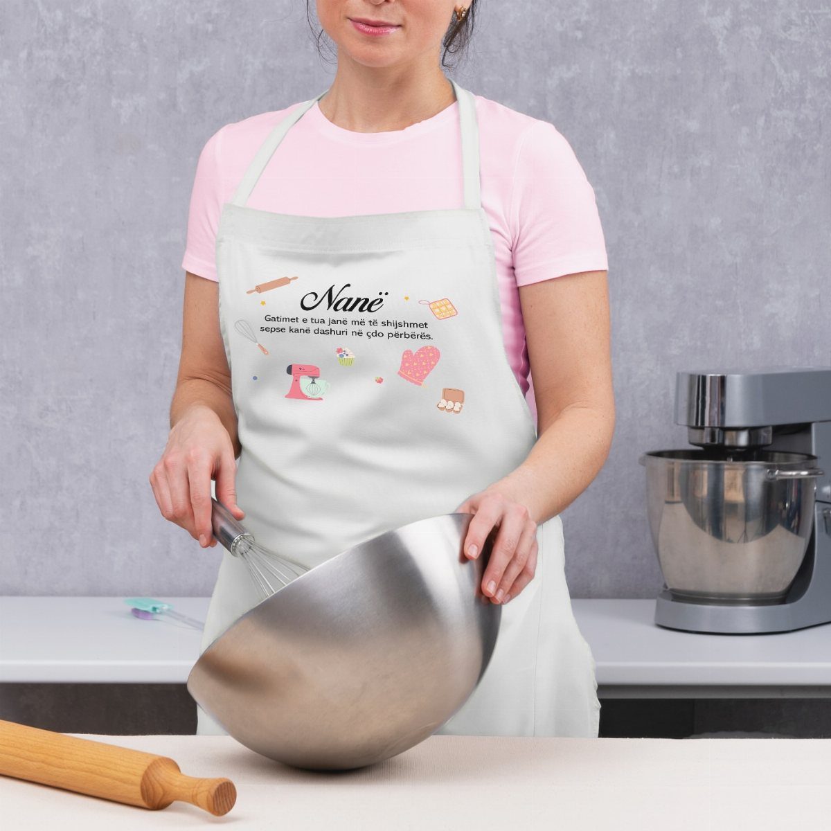 Woman wearing a custom white apron while whisking ingredients in a metal bowl.