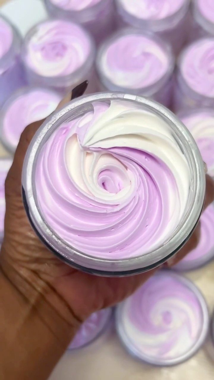 Swirled purple and white body butter in a clear jar held by a hand.
