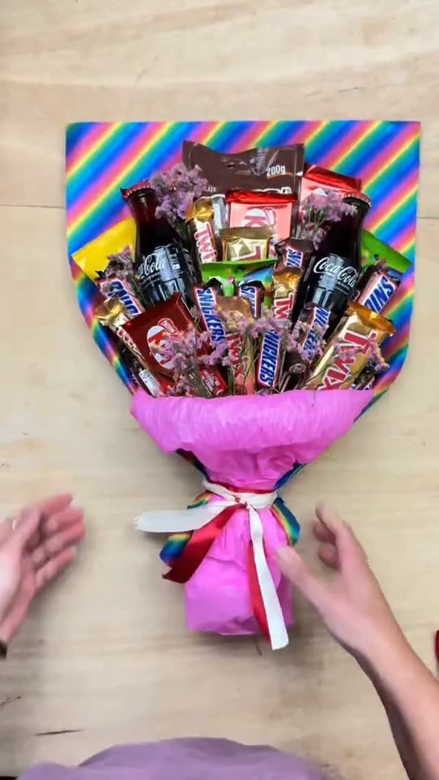 Chocolate and soda bouquet wrapped in pink paper on a wooden table.