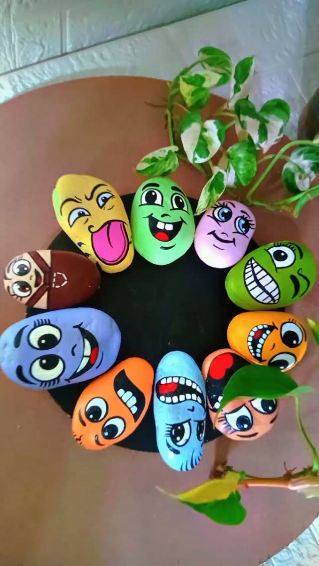 Colorful painted rocks with cartoon faces arranged in a circle near a plant.