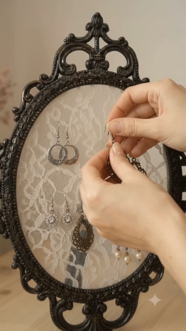 Hands arranging silver and bronze earrings on lace inside an ornate black frame.