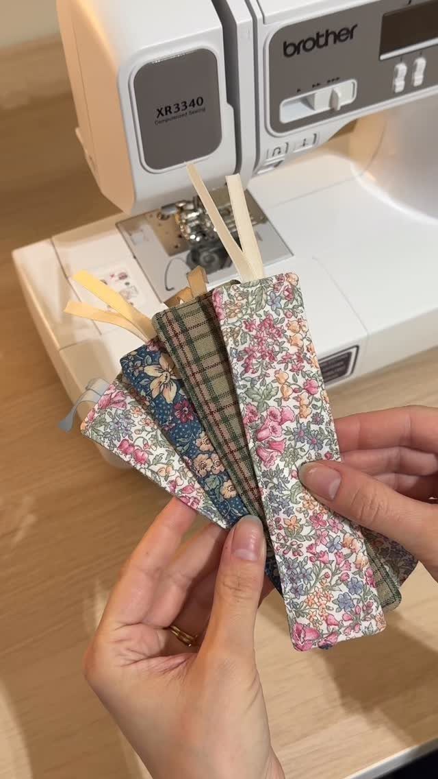 Fabric bookmarks with floral and plaid patterns held in front of a sewing machine.