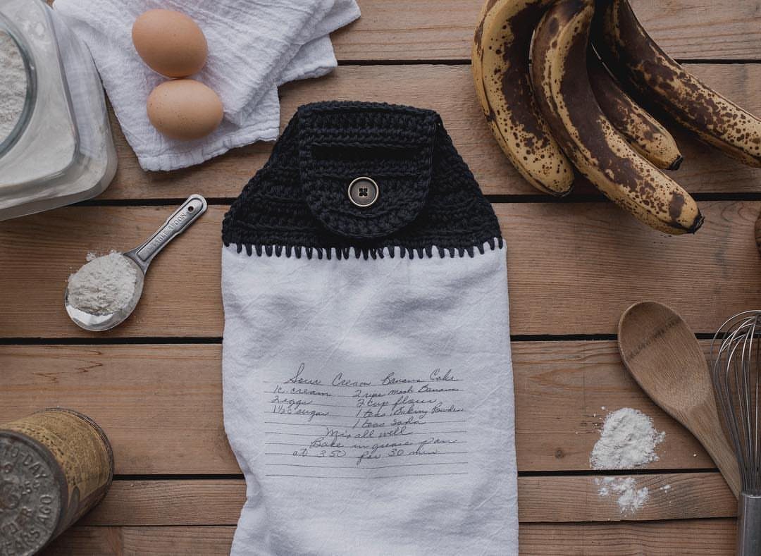 White kitchen towel with handwritten recipe and black crochet top on wooden table
