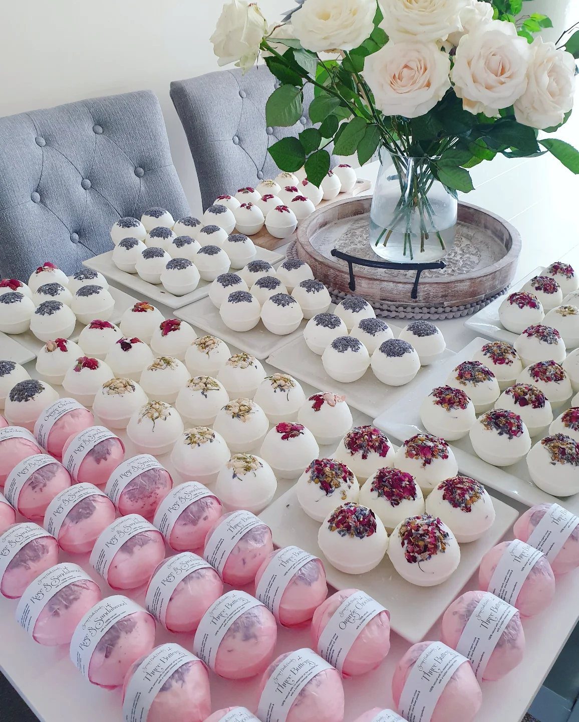 White and pink bath bombs with dried petals arranged on white trays.