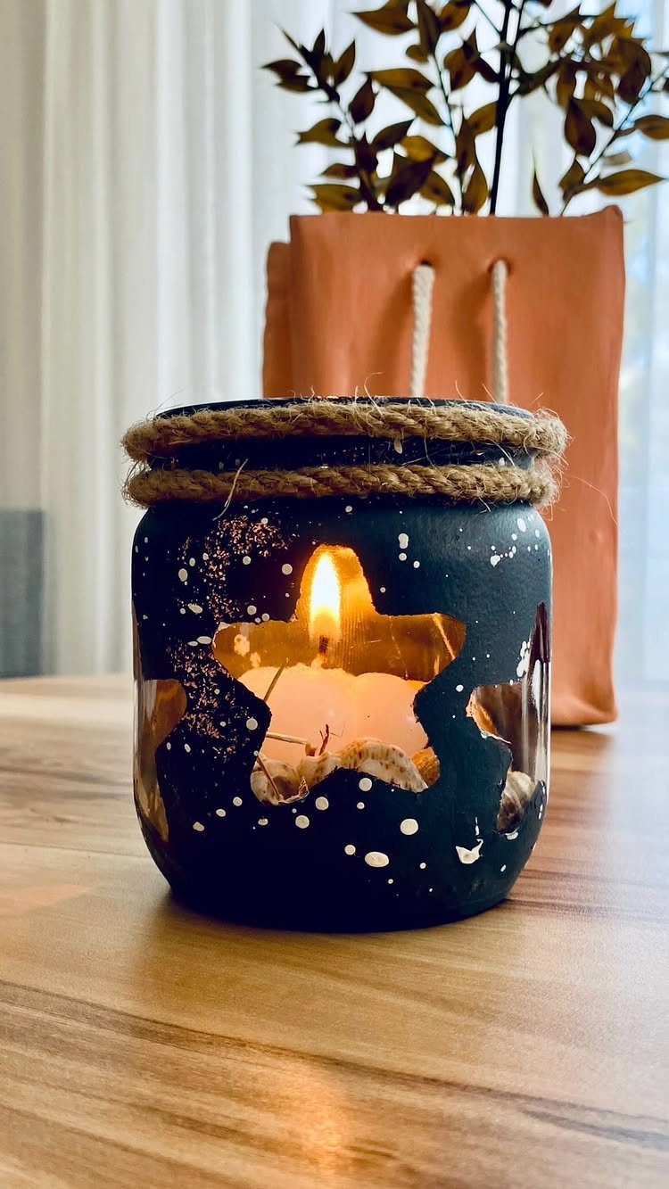 Lit candle in a dark blue painted mason jar with star cutouts and twine.