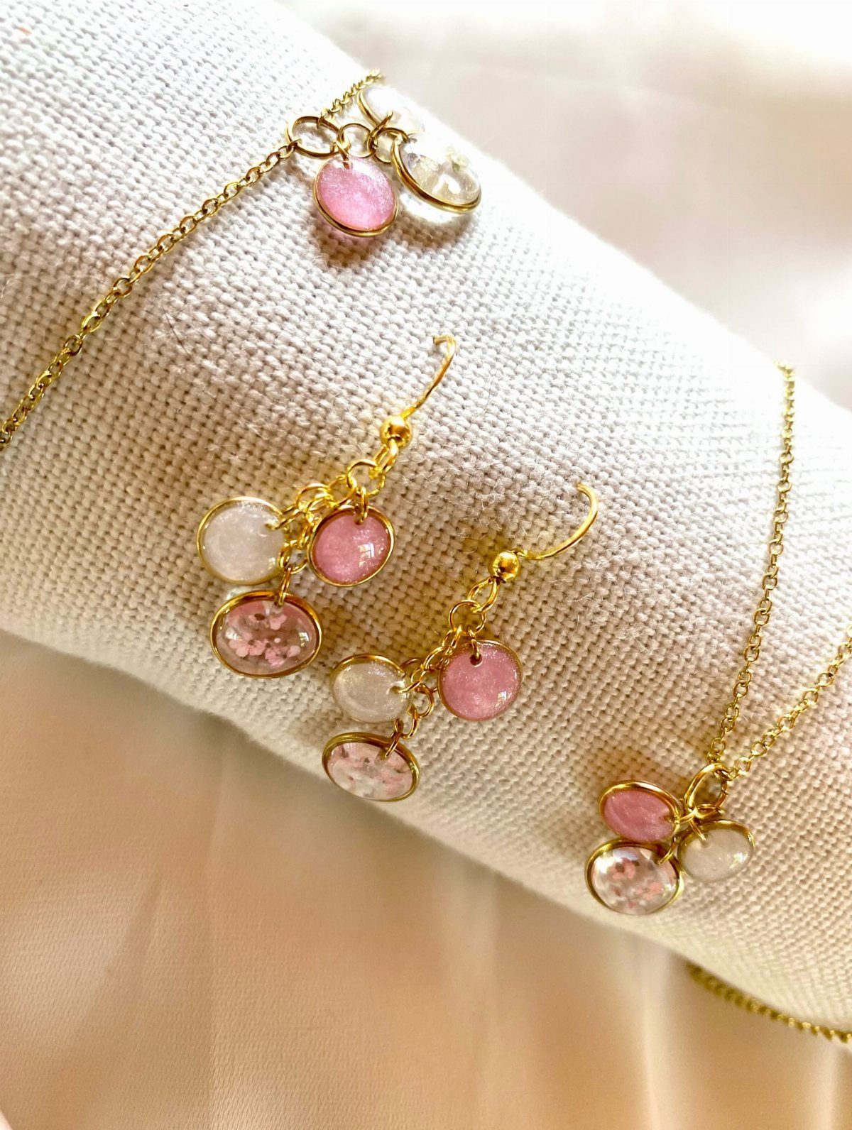 Gold jewelry set with pink and white round charms on white fabric.