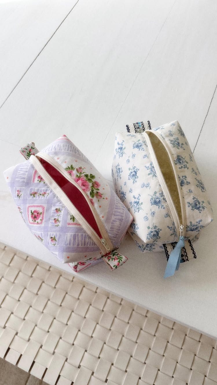 Two floral fabric zipper pouches, one purple and one white, on white wood.