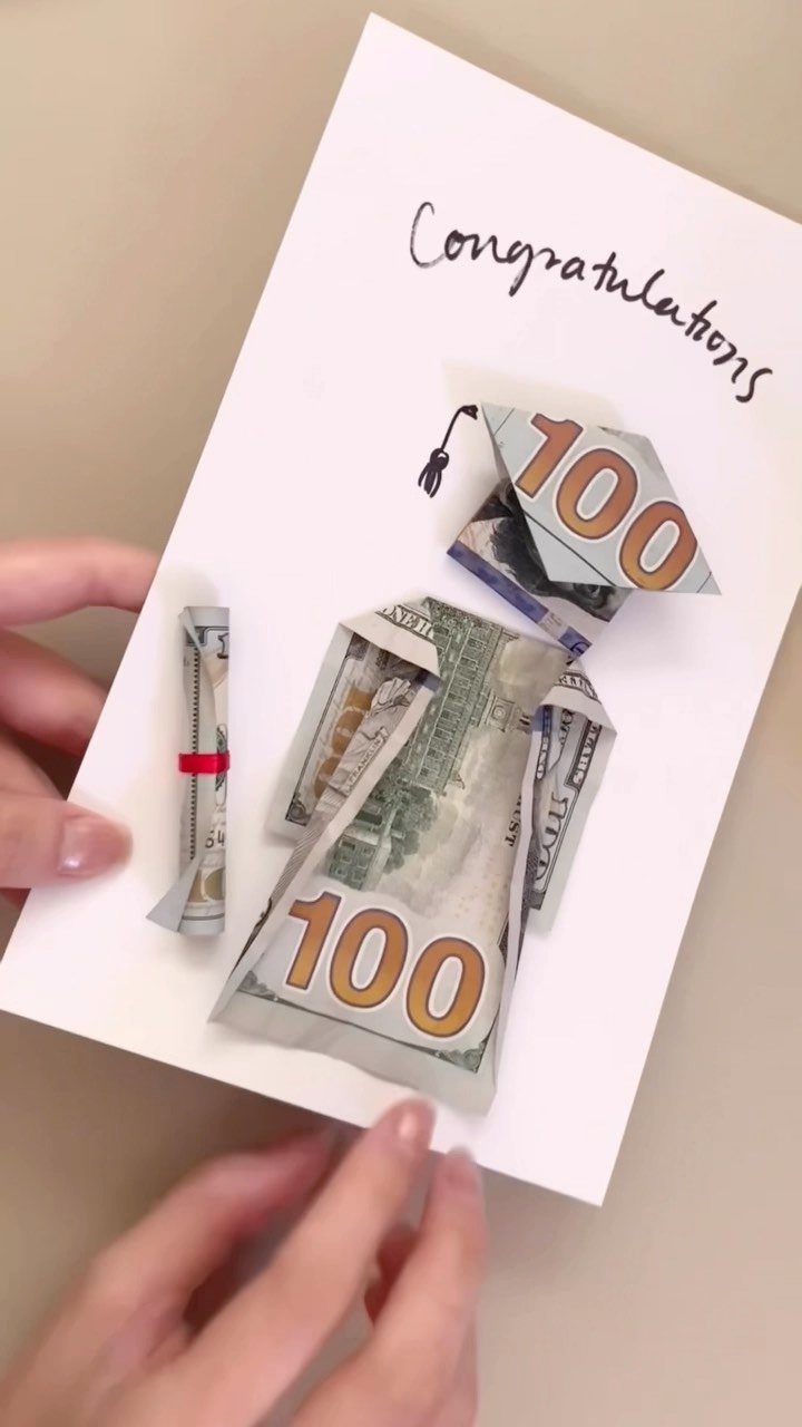 Graduation gown and cap made from folded hundred dollar bills on a card.