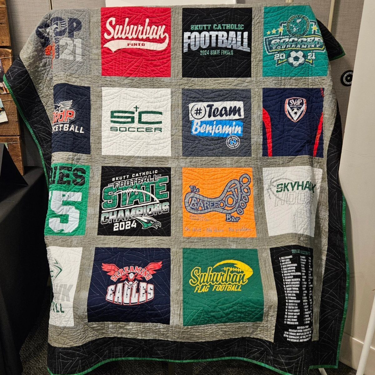 T-shirt quilt featuring various sports team logos and names in colorful fabric squares.