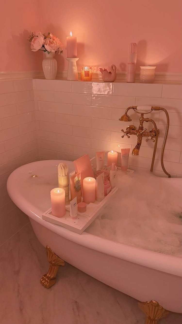 White bathtub tray holding pink candles and skincare products in a pink bathroom.