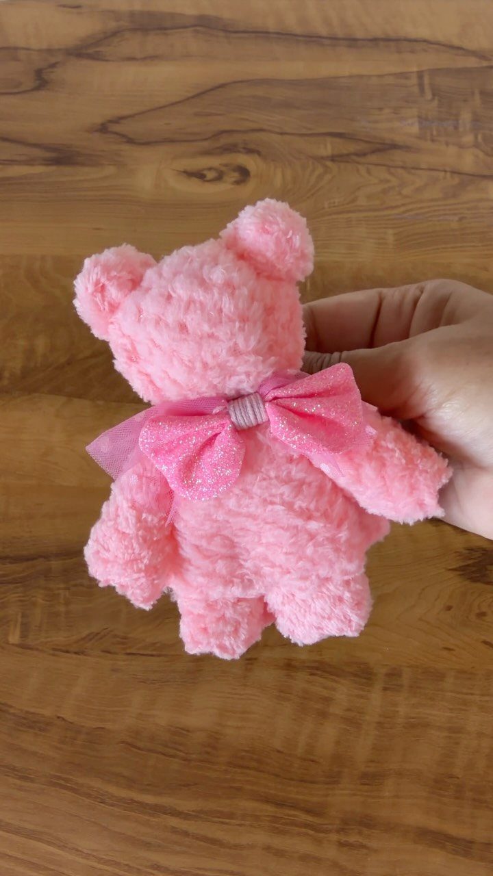 Small pink crocheted teddy bear with a sparkly bow held by a hand.
