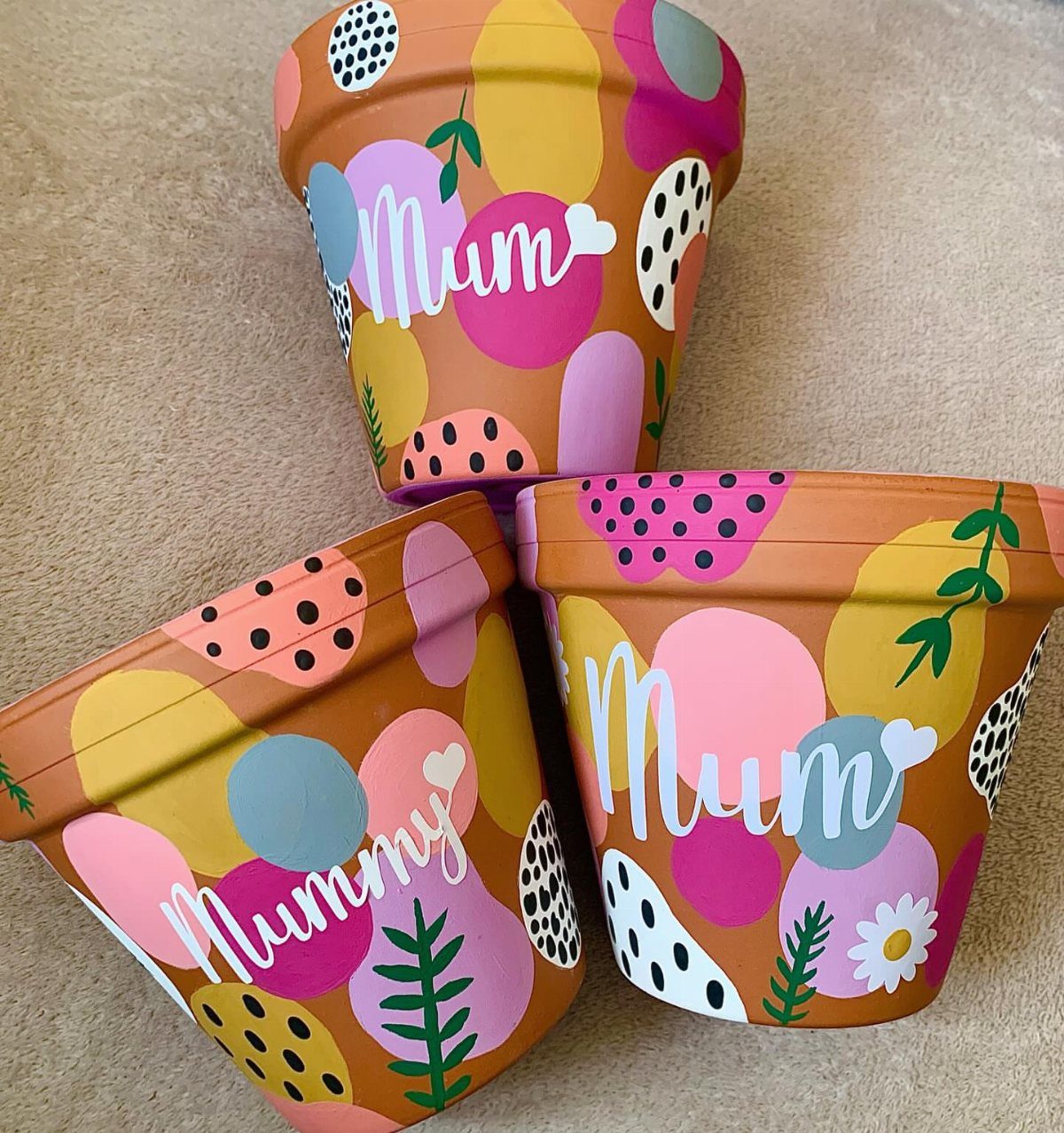 Three terracotta flower pots painted with colorful abstract shapes and the word Mum.