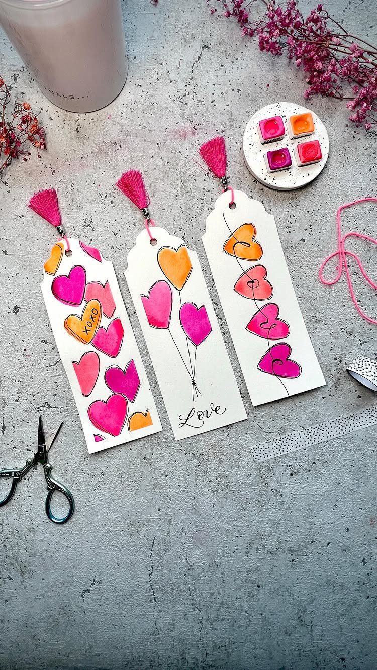 Hand-painted bookmarks with colorful hearts and pink tassels on a grey stone surface.
