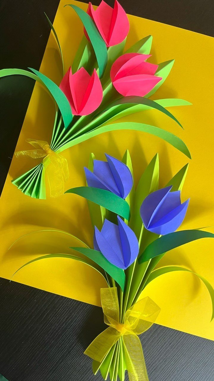 Two paper flower bouquets with pink and blue tulips on yellow paper.