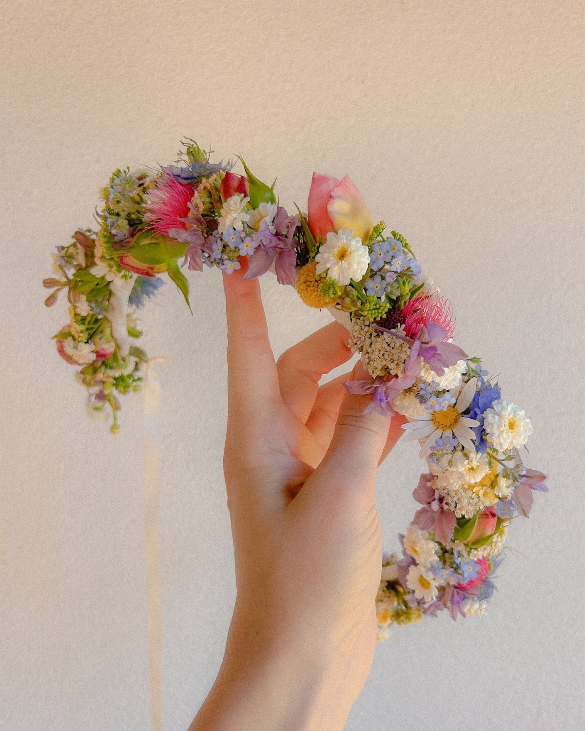 Flower crown with colorful blossoms held by a hand against a white background