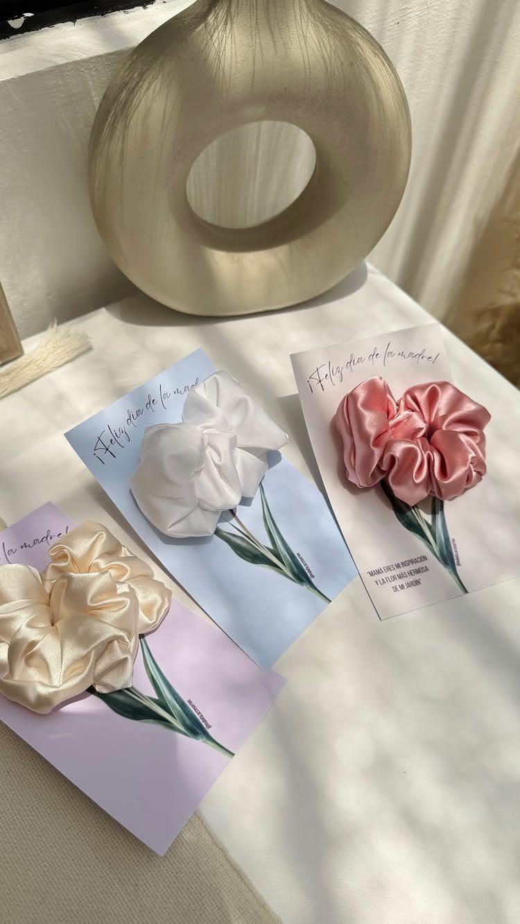 Three fabric hair scrunchies in cream, white, and pink on floral cards.