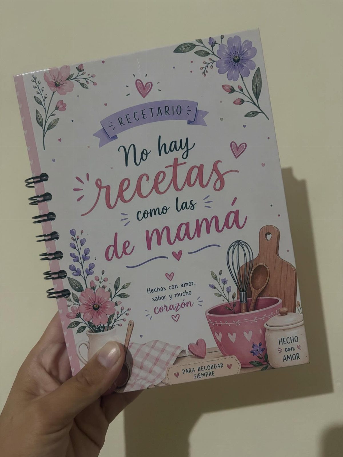 Spiral-bound recipe book with floral cover and Spanish text held by a hand.