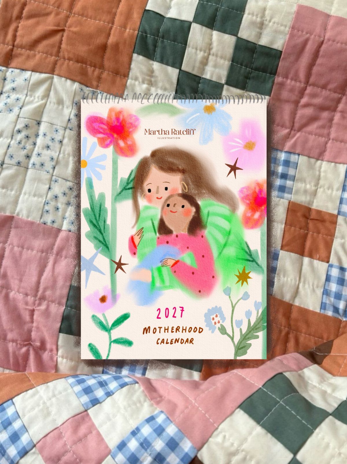 Spiral-bound motherhood calendar with illustration of mother and child on patchwork quilt