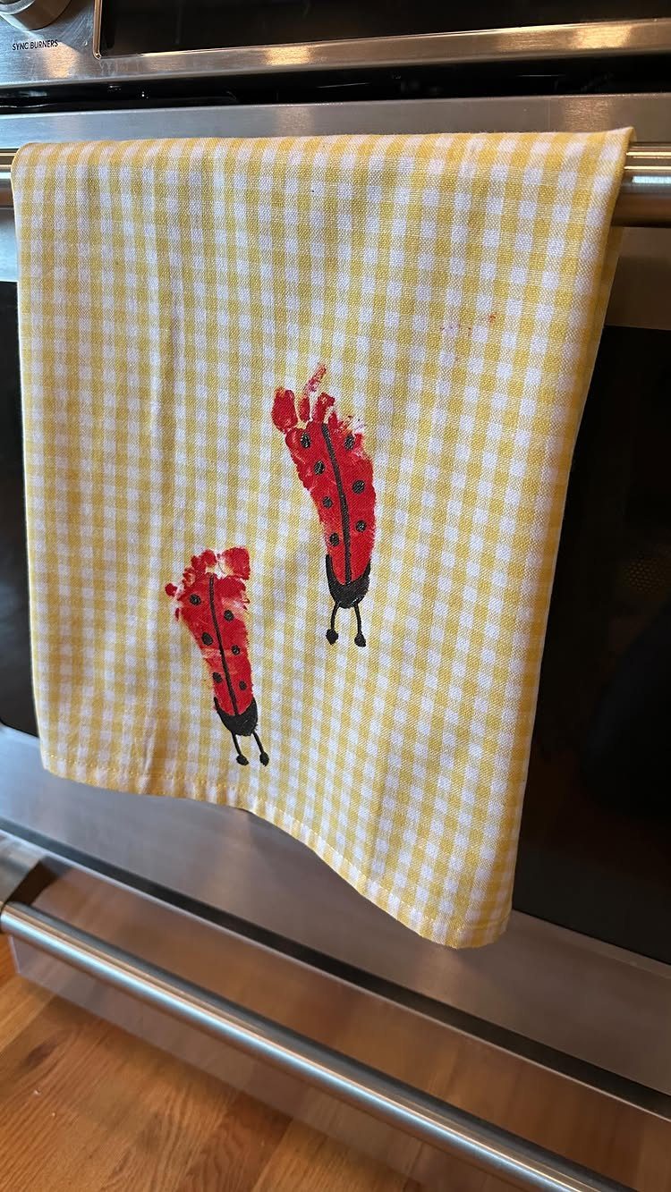 Yellow checkered kitchen towel with two red ladybugs painted on it hanging on oven.