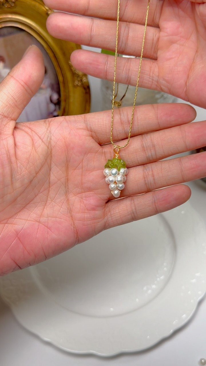 Gold chain necklace with a grape pendant made of white pearls and green beads.