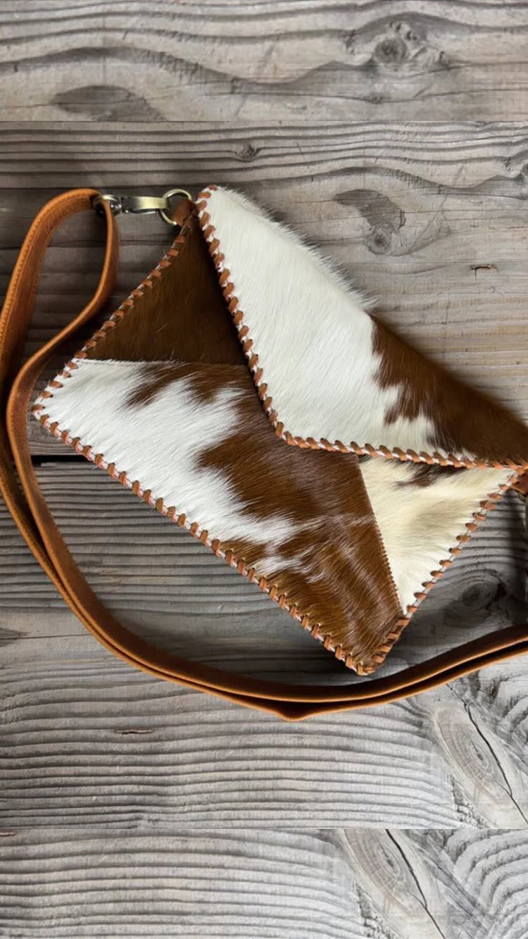 Cowhide leather envelope clutch bag with a brown strap on a wooden background