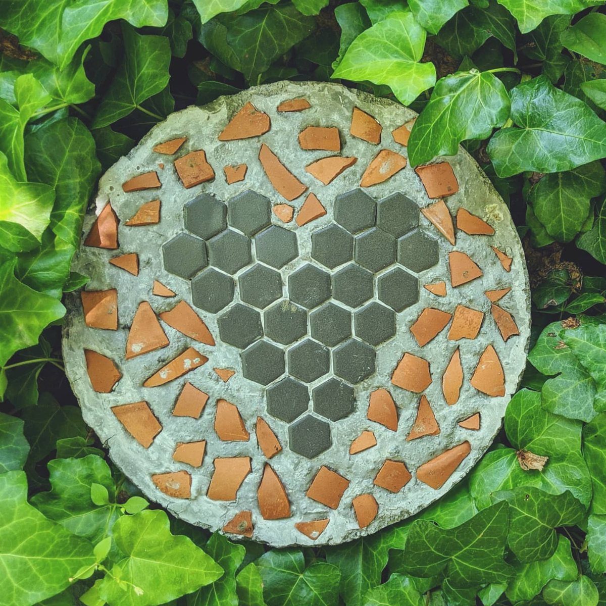 Concrete stepping stone with a grey tile heart and orange shards in ivy
