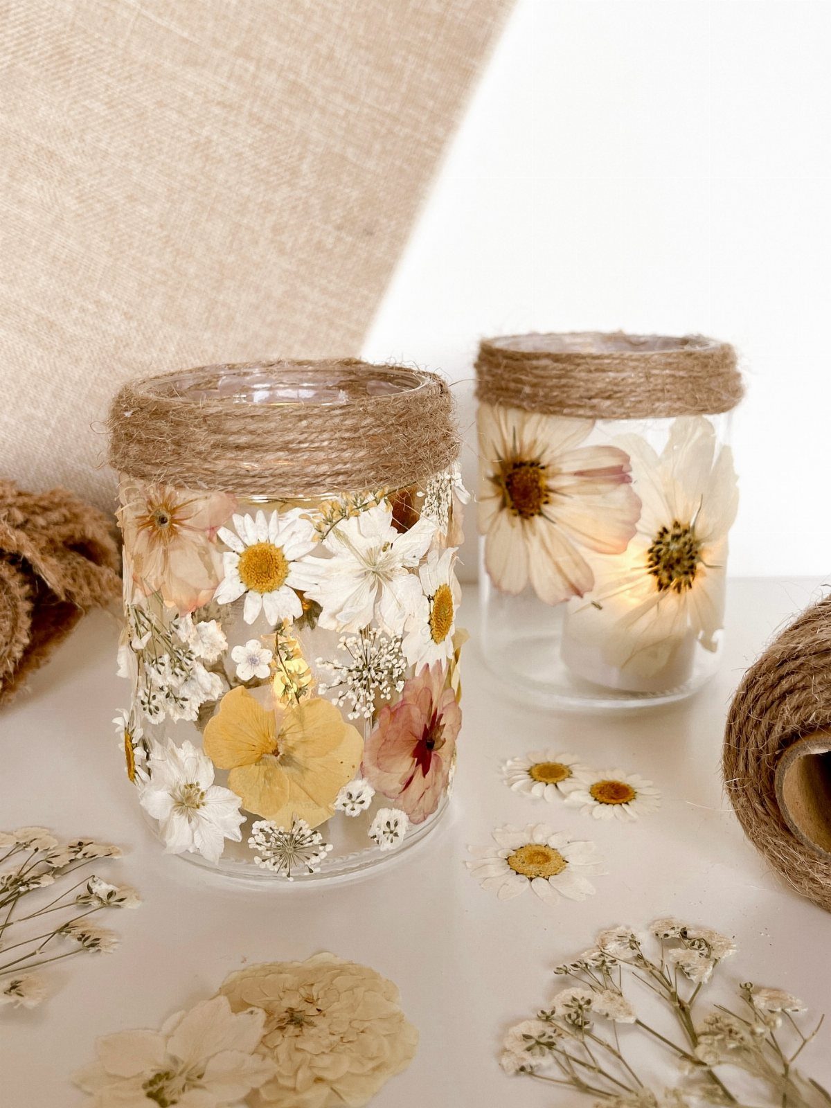 Two glass jars decorated with pressed flowers and twine rims on a white surface.