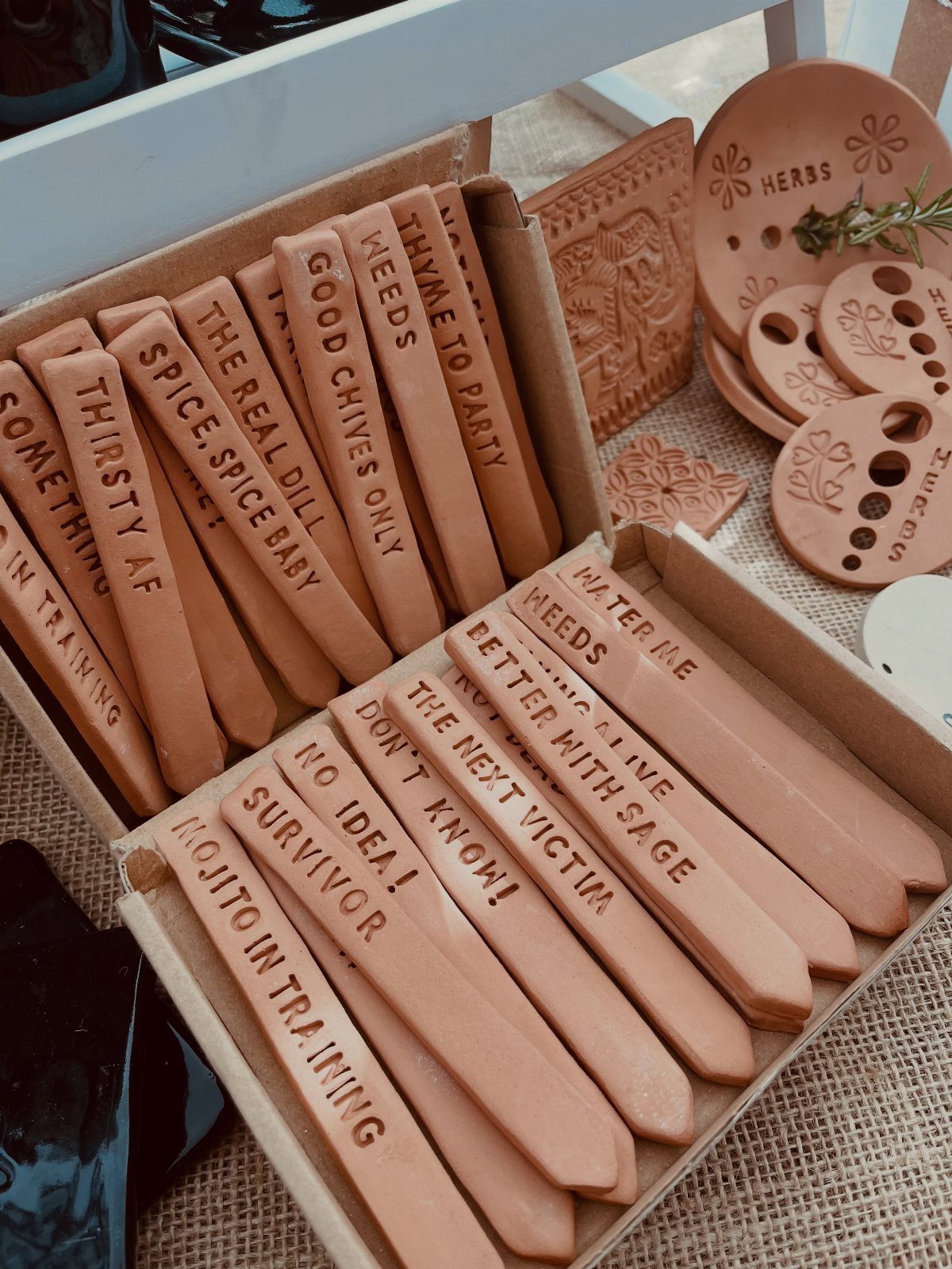 Terracotta clay plant markers with engraved text arranged in a cardboard box.