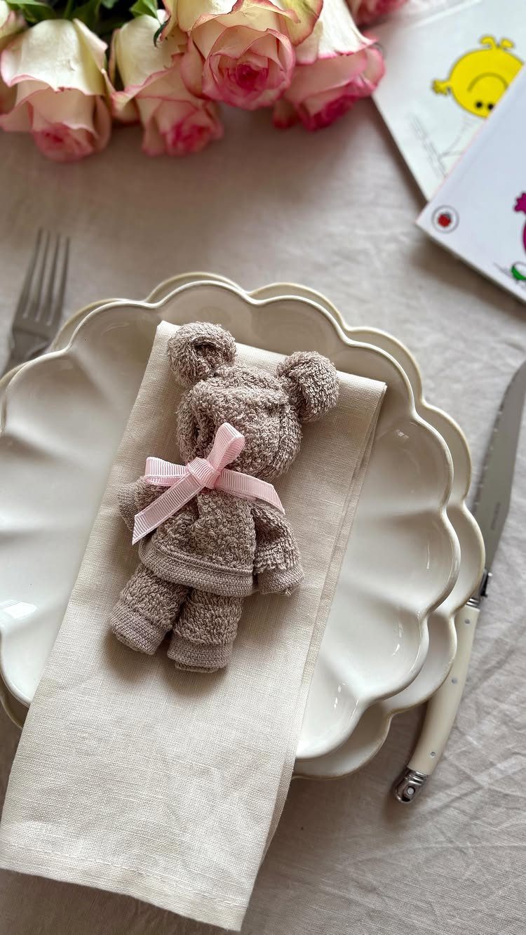 Towel teddy bear with pink bow on a white plate and linen napkin