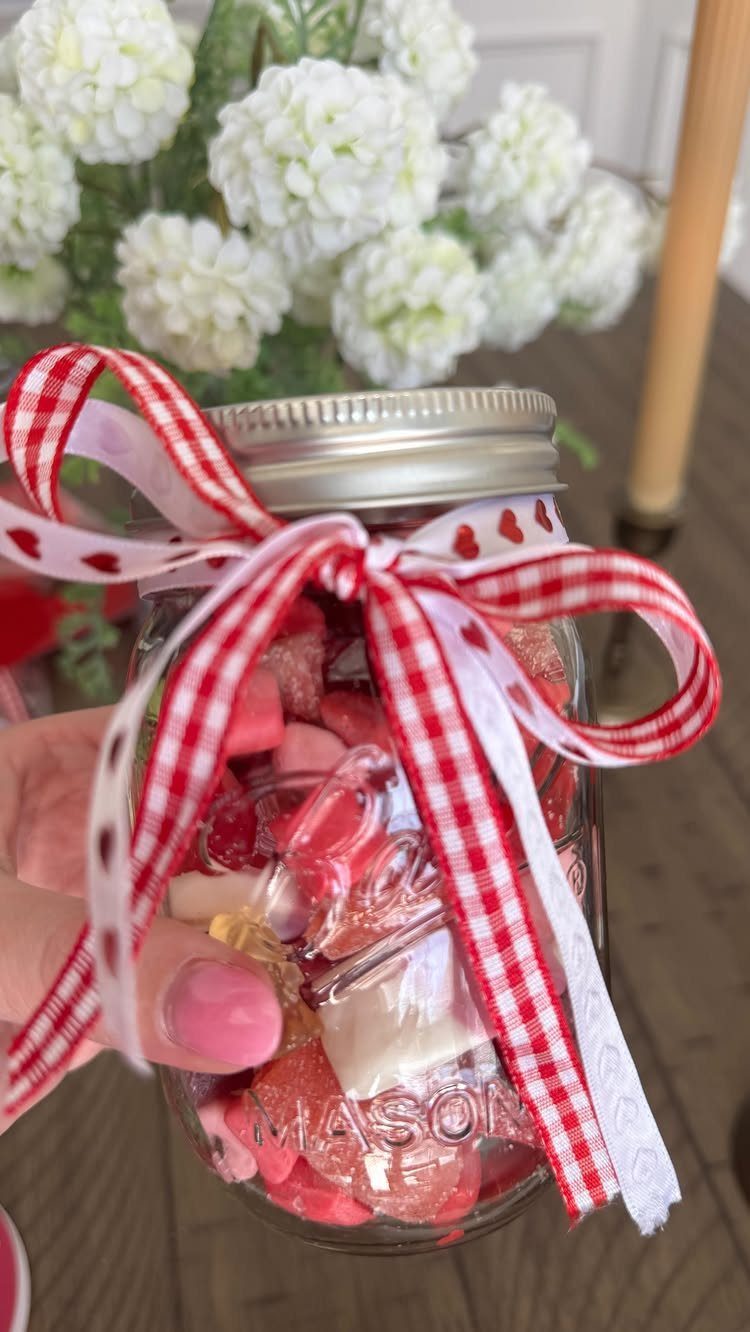 Mason jar filled with red and white candies tied with festive ribbons.