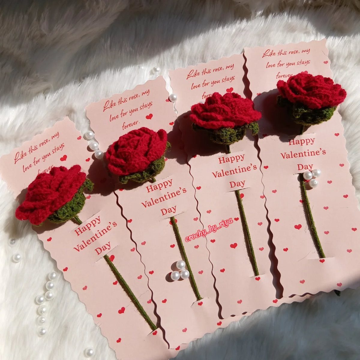 Red crochet roses on pink Valentine's Day cards resting on white faux fur.
