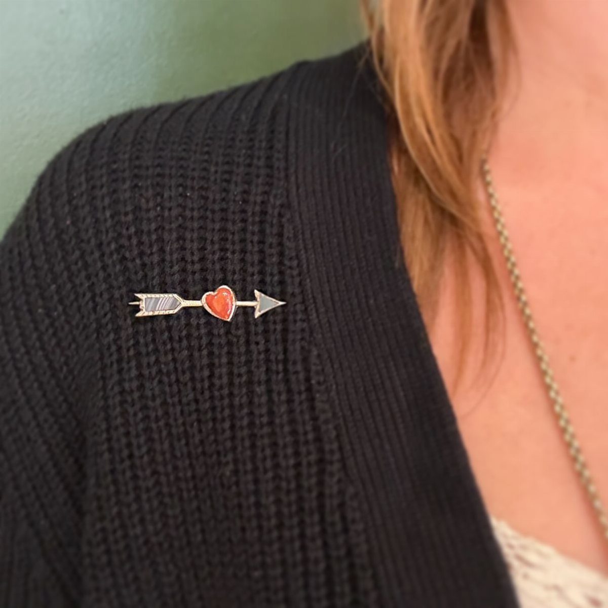 Silver arrow pin with a red heart pinned to a black ribbed sweater.