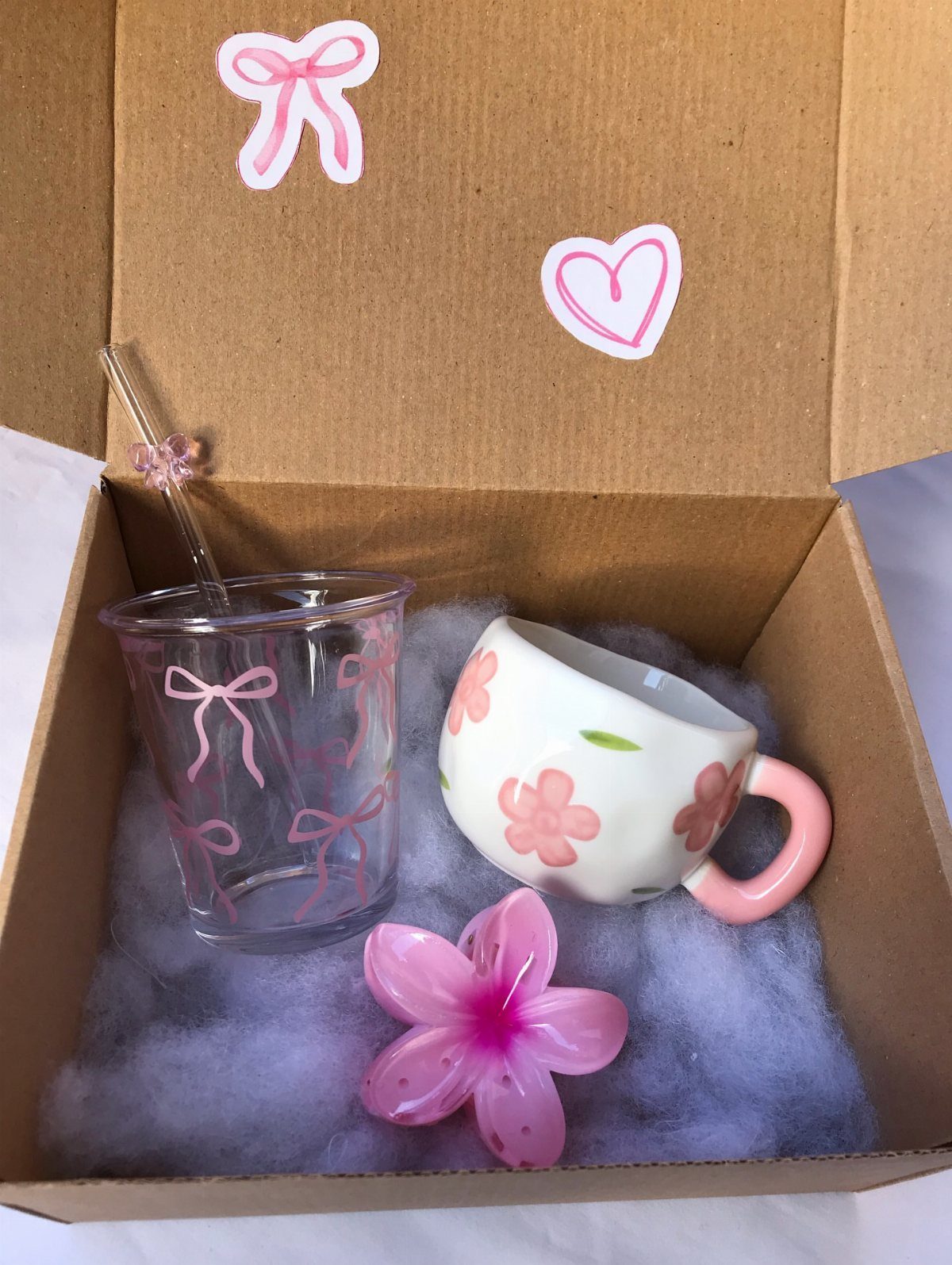 Gift box with a decorated glass cup, floral ceramic mug, and pink flower.