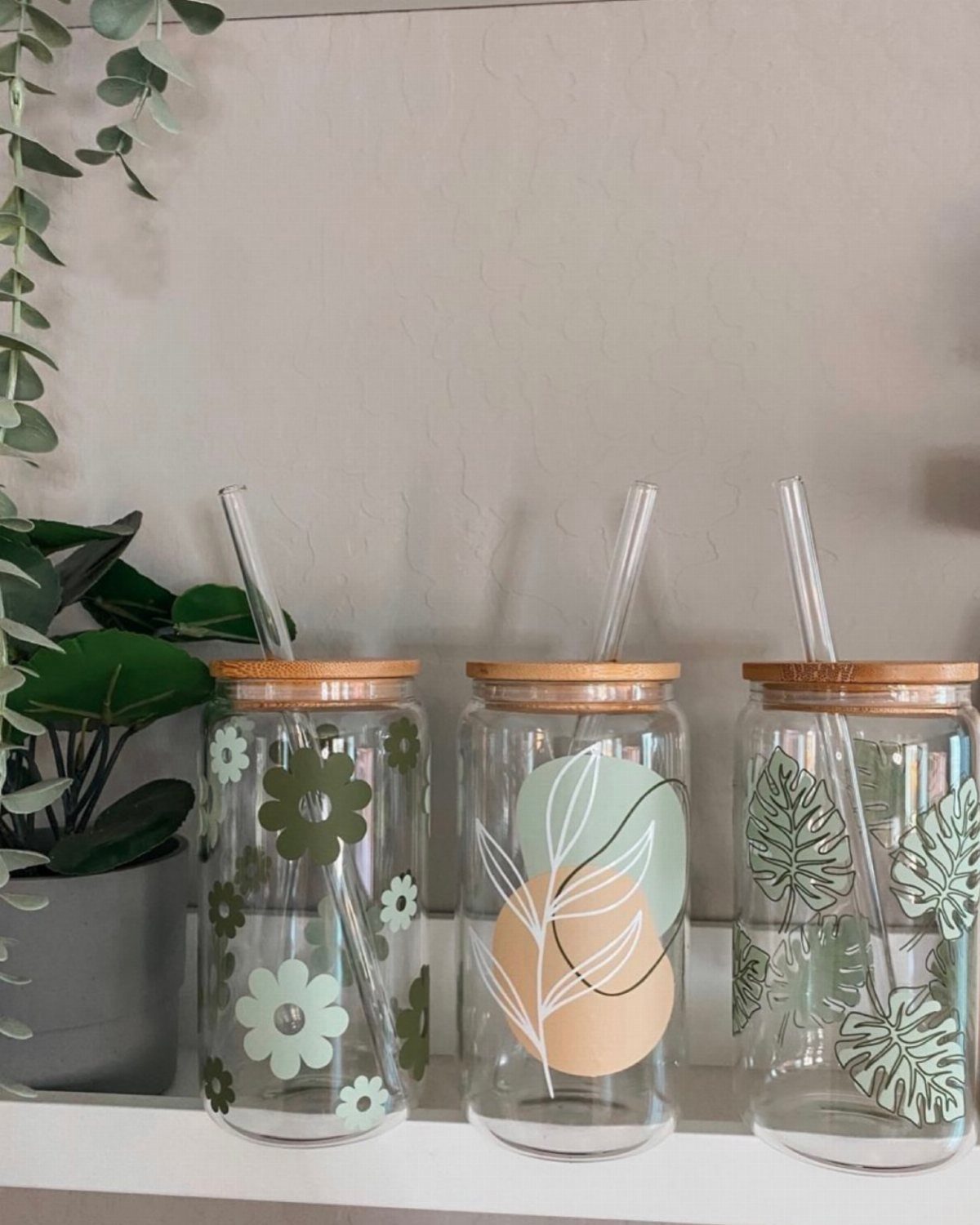 Three glass jars with bamboo lids and botanical decals on a white shelf.