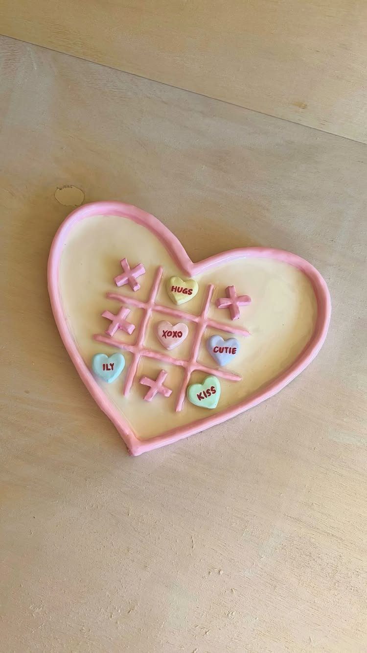 Heart-shaped coaster with a tic-tac-toe game using candy conversation hearts on wood.