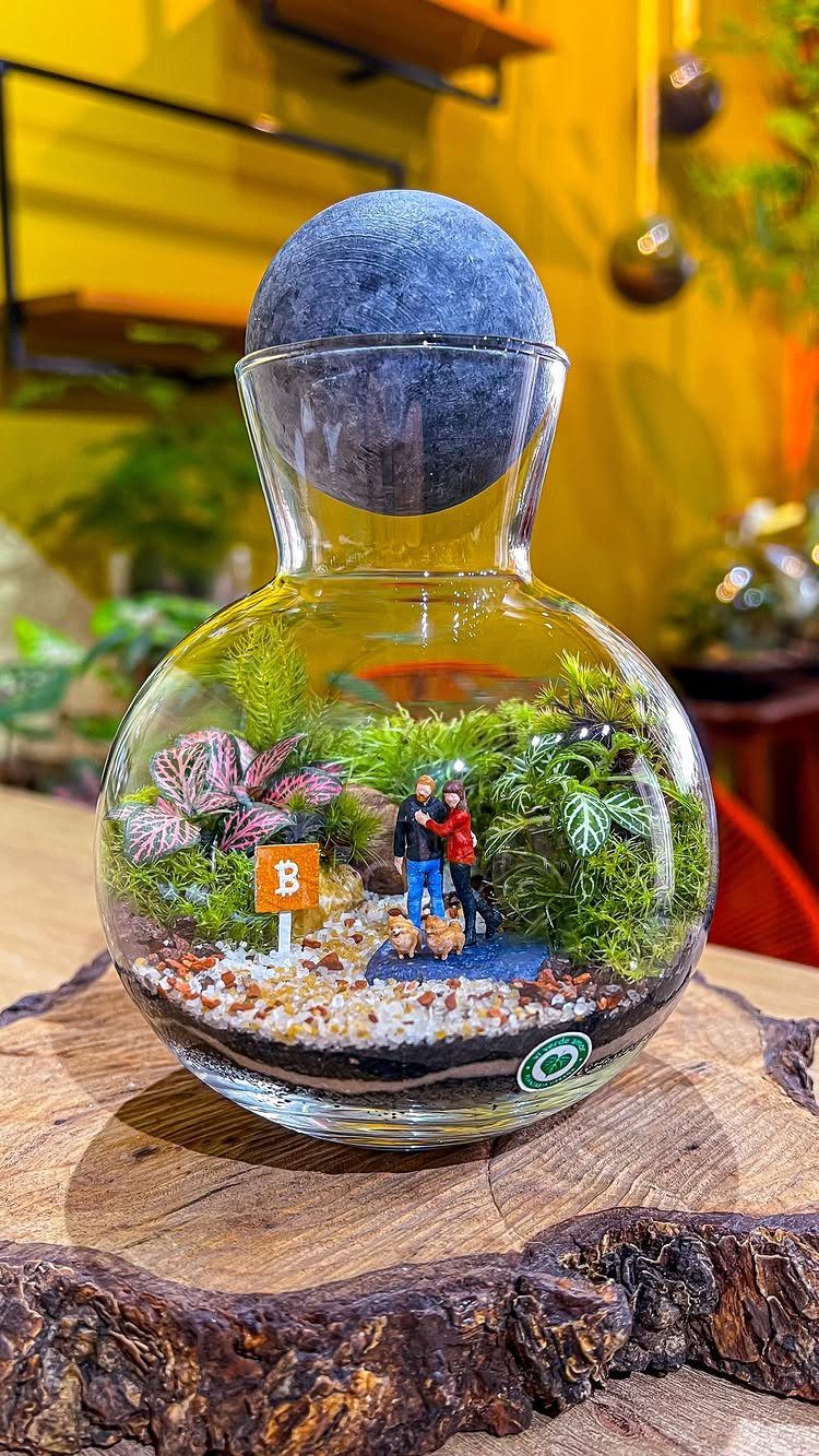 Glass flask terrarium with miniature couple and plants on a wooden base