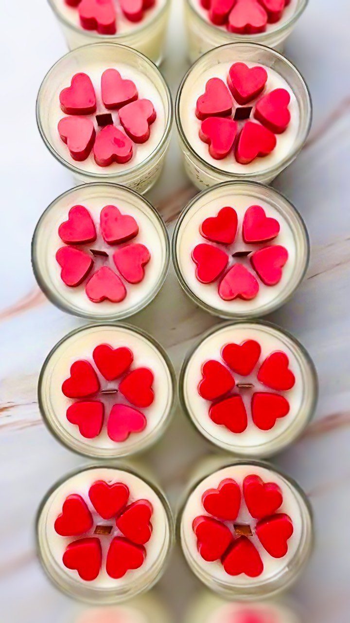 White wax candles in glass jars topped with red heart-shaped wax pieces.