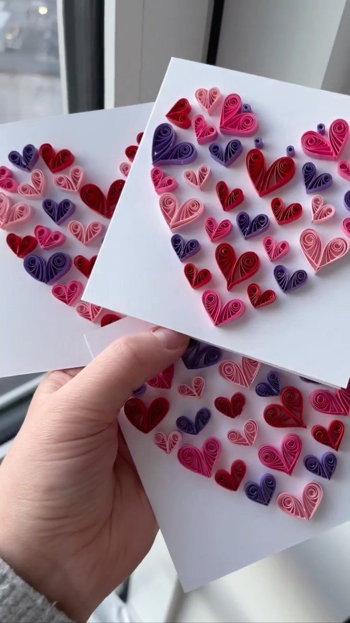 Hand holding white cards decorated with coiled paper hearts in red and purple.