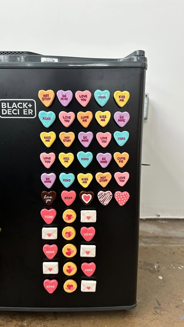 Heart-shaped and envelope magnets arranged in a heart pattern on a black mini fridge.