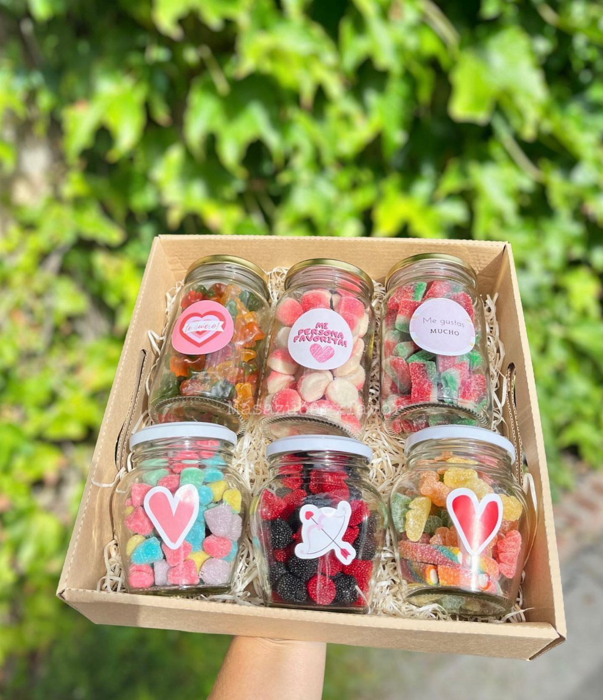 Six jars of colorful gummy candies with heart stickers in a gift box.