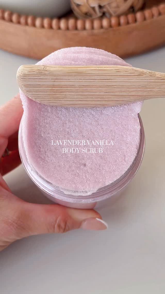 Lavender vanilla body scrub in a clear jar with a wooden spatula.