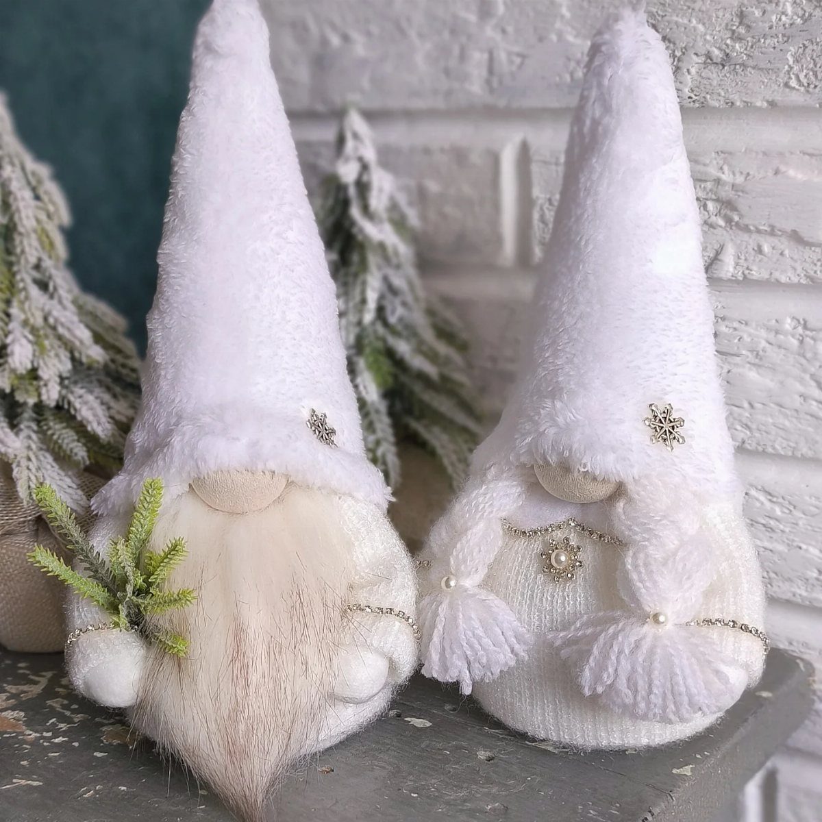 Two white plush gnome ornaments with tall hats and beards near frosted trees.