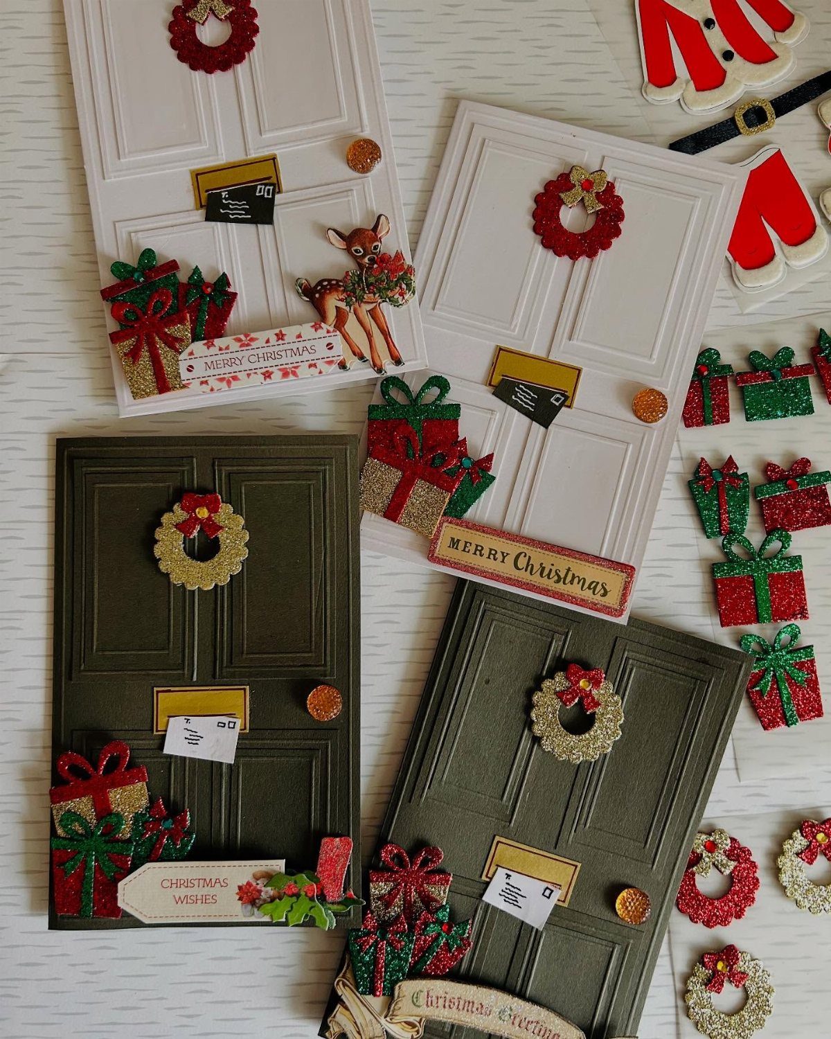 Handmade Christmas cards shaped like doors with miniature wreaths and tiny gift boxes.