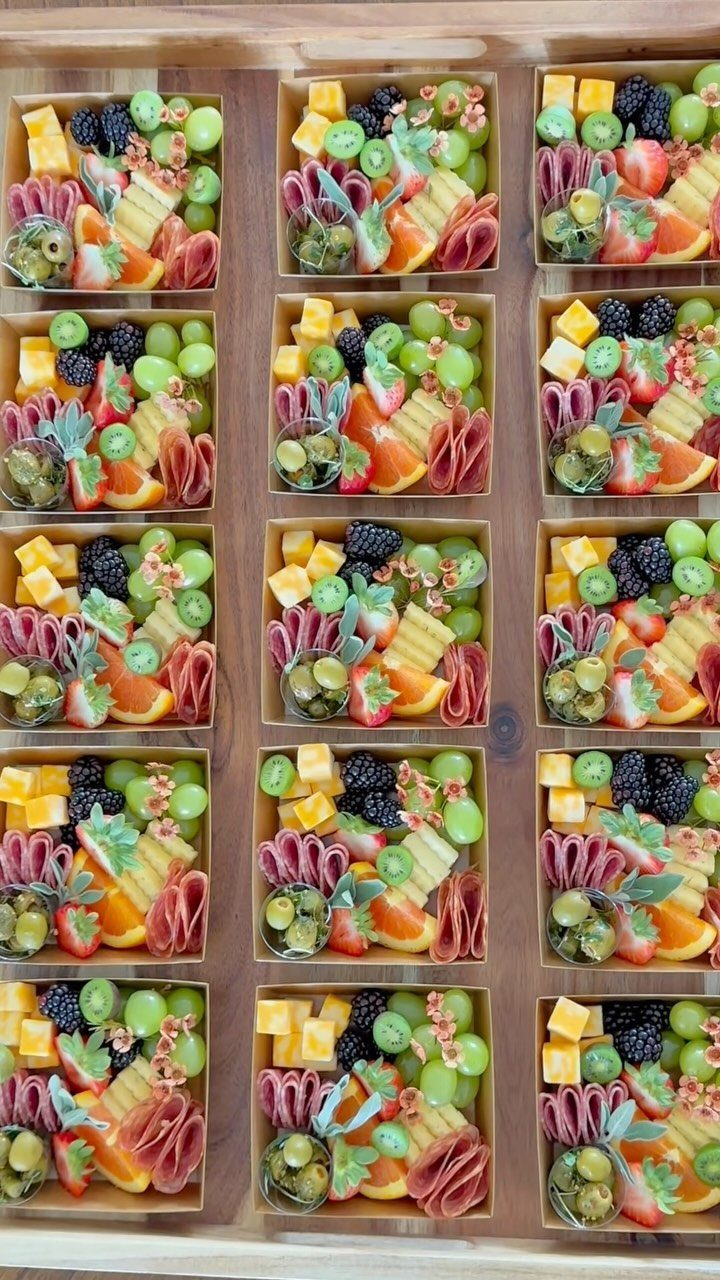 Individual charcuterie boxes filled with cheese, meats, and fruit in a wooden tray.