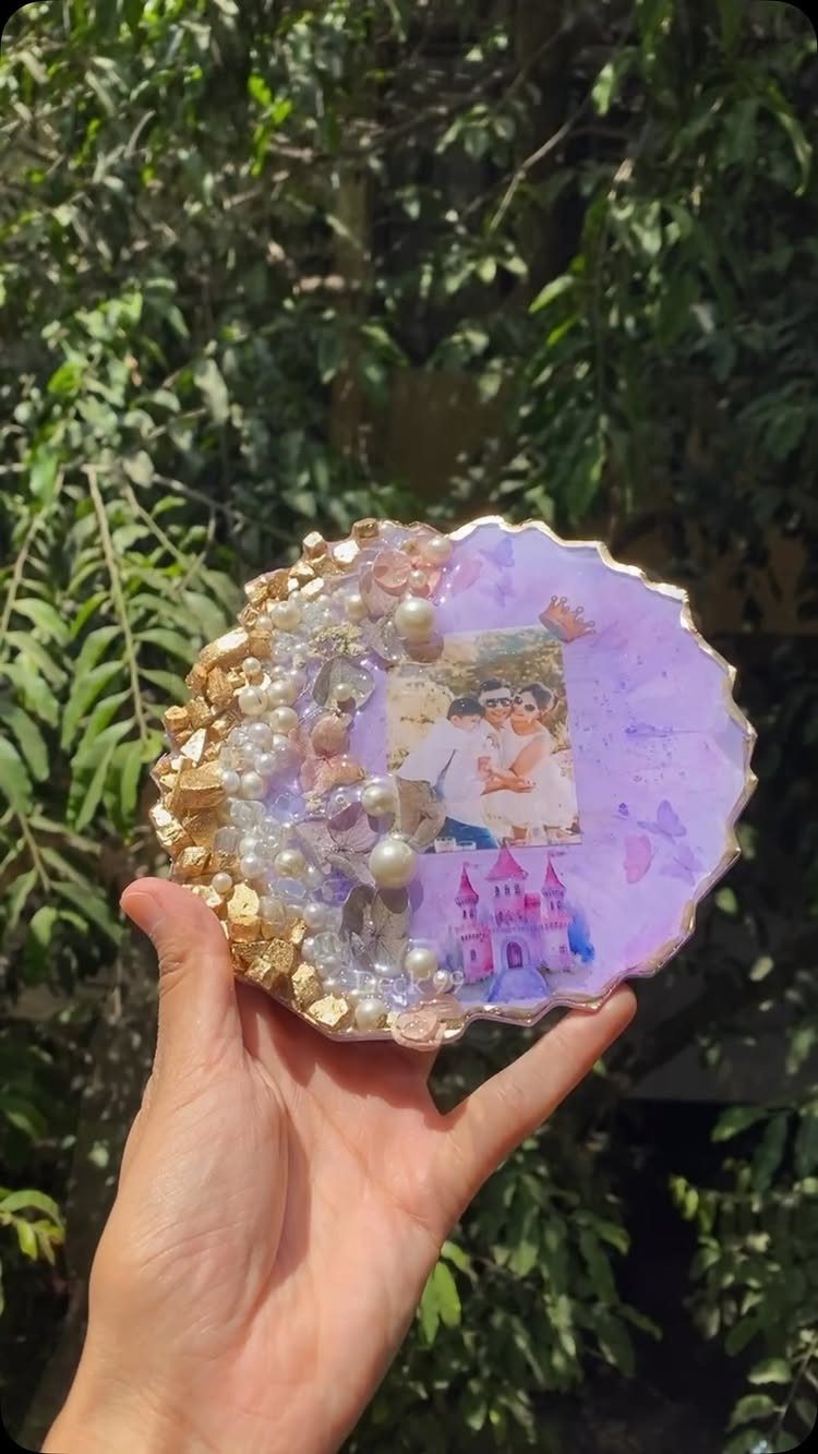 Purple resin coaster with embedded photos, gold flakes, and pearls held by hand.