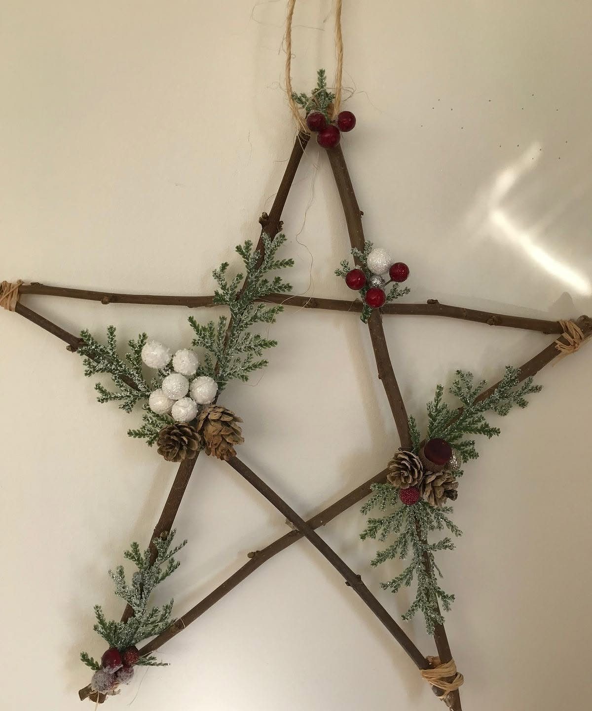 Twig star decoration with evergreen sprigs, berries, and pinecones hanging on a wall