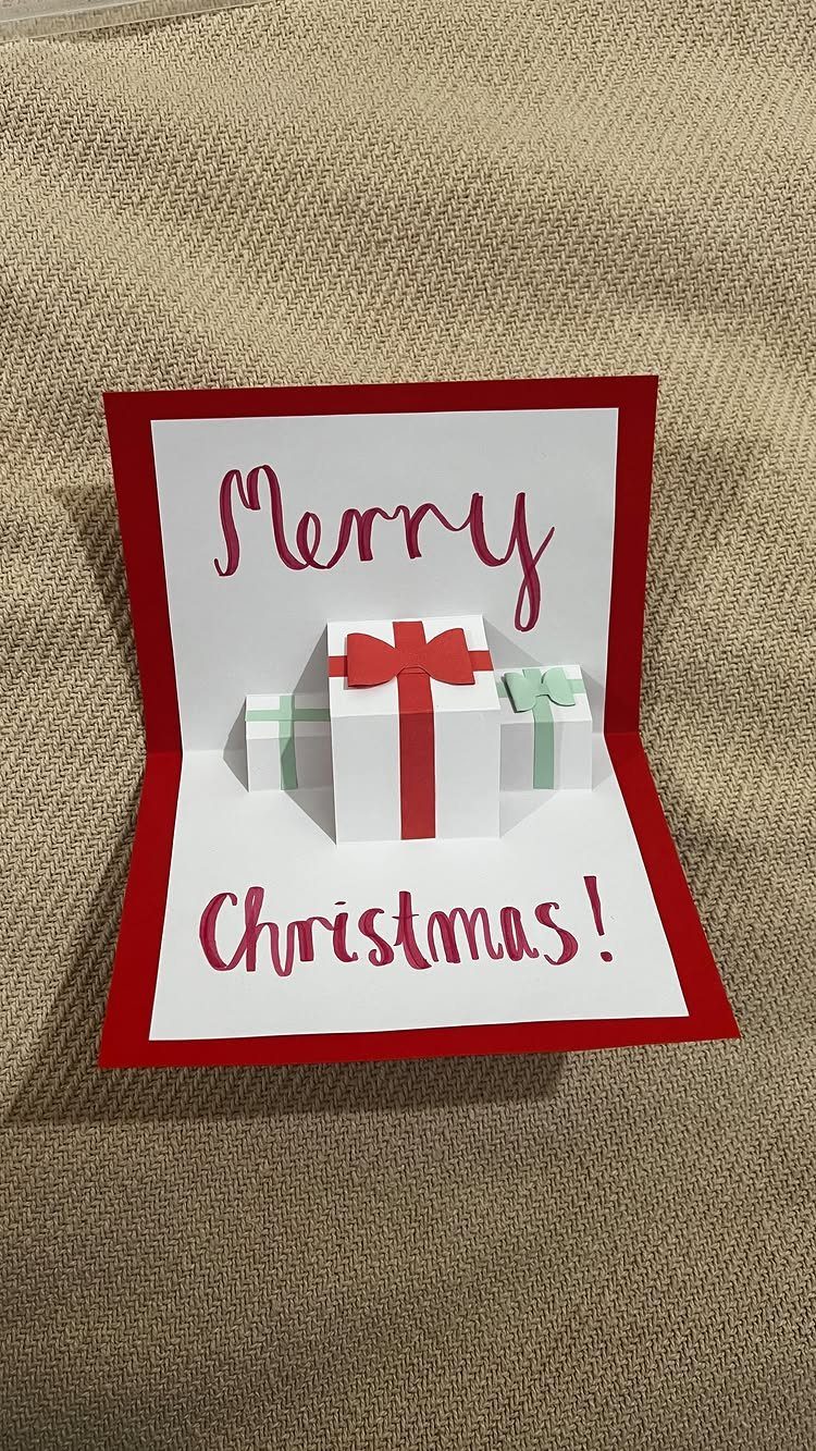Pop-up Christmas card with three small paper gift boxes and red cursive text.