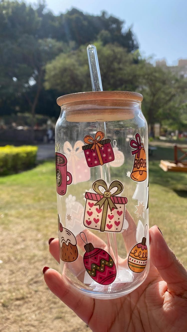 Glass jar with Christmas stickers and wooden lid held in a hand outdoors.