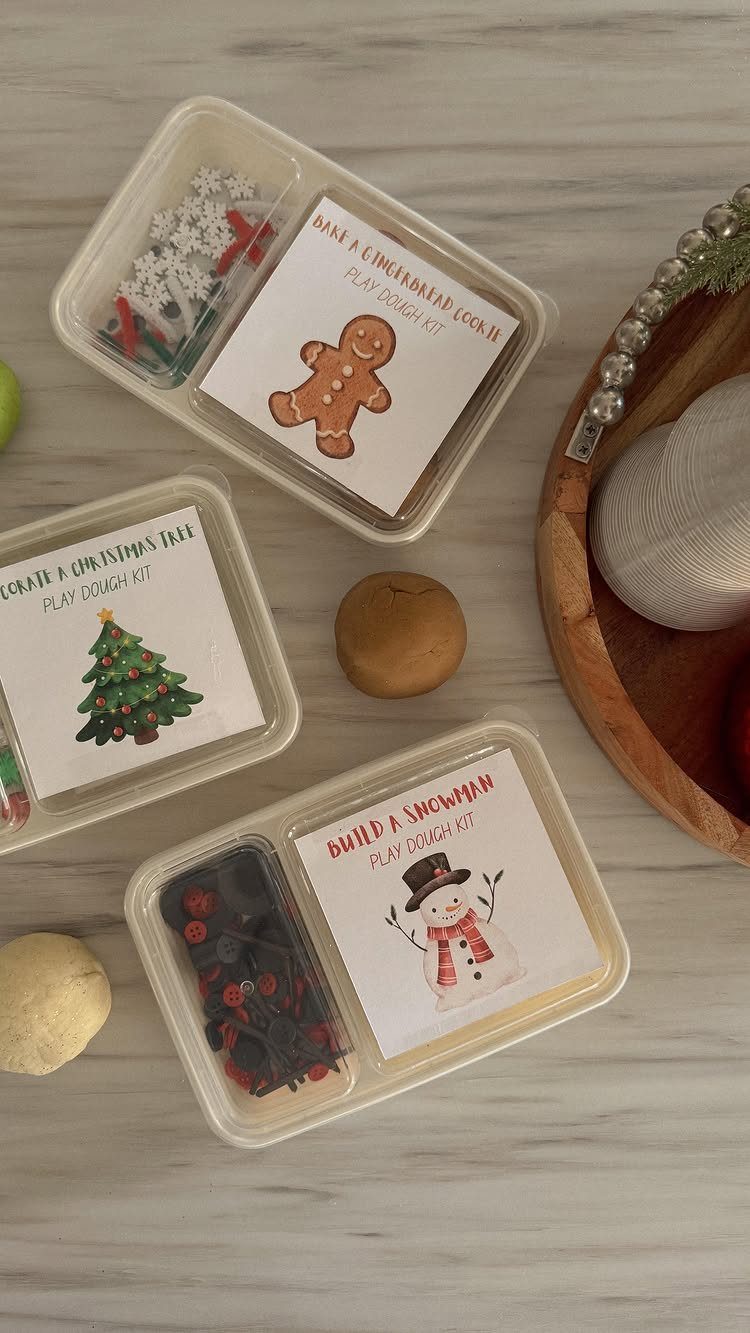 Three holiday-themed DIY playdough kits in clear plastic containers on marble surface.