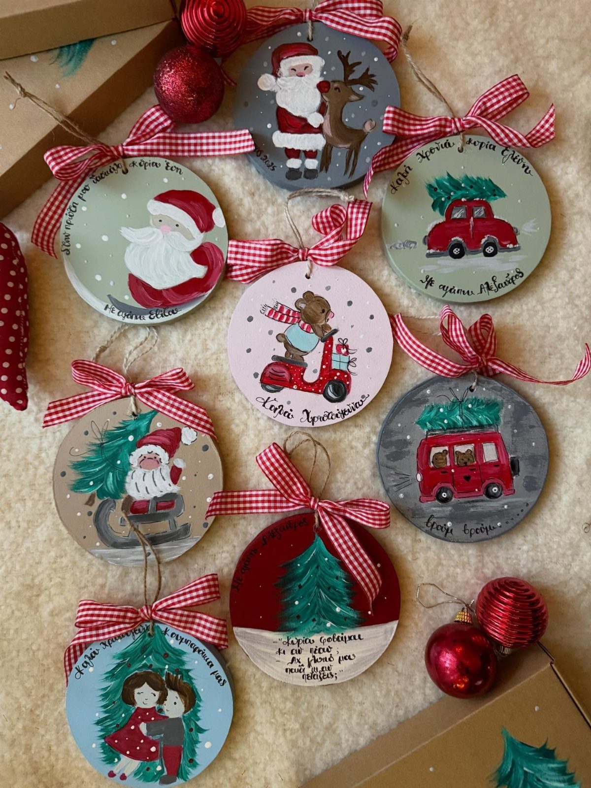 Hand-painted wooden Christmas ornaments with red checkered ribbons on a white fluffy background.